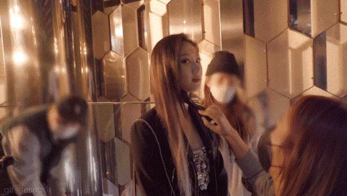 a woman is getting her hair done in front of a mirror while another woman looks on