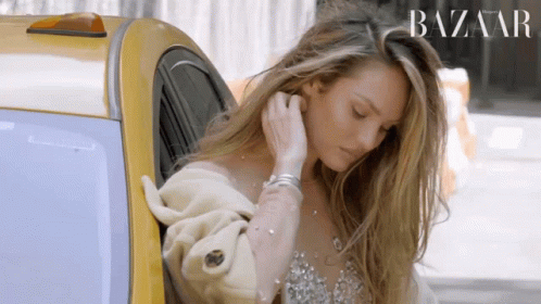 A Woman Is Getting Out Of A Taxi With A Harper 'S Bazaar Logo Behind Her GIF