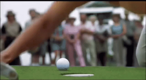 A Woman Is Hitting A Golf Ball Into A Hole . GIF