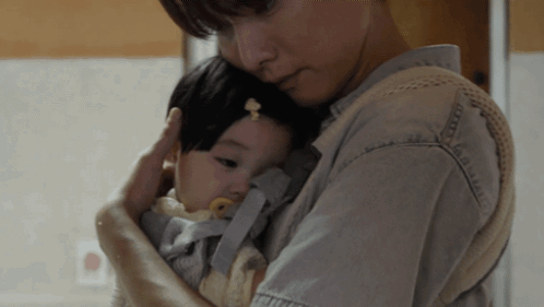 A Woman Is Holding A Baby In A Carrier GIF