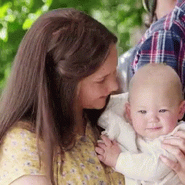 A Woman Is Holding A Baby In Her Arms And The Baby Is Smiling For The Camera . GIF