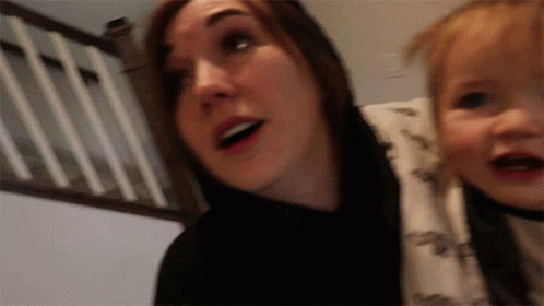 A Woman Is Holding A Baby In Her Arms And The Baby Is Wearing A Dinosaur Shirt GIF