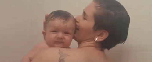 A Woman Is Holding A Baby In Her Arms While Taking A Bath . GIF