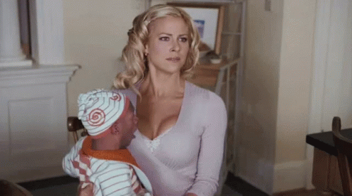 A Woman Is Holding A Baby Wearing A Hat With A Swirl On It GIF