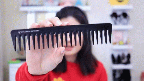 A Woman Is Holding A Black Comb That Says Ghd GIF