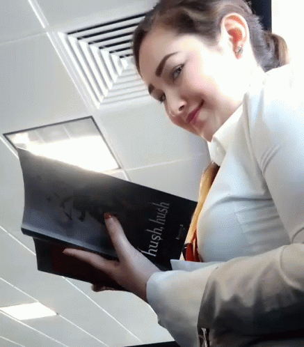A Woman Is Holding A Book That Says Hush Hush On It GIF