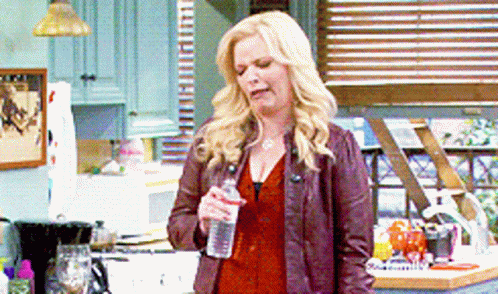 A Woman Is Holding A Bottle Of Water In Her Hand In A Kitchen GIF