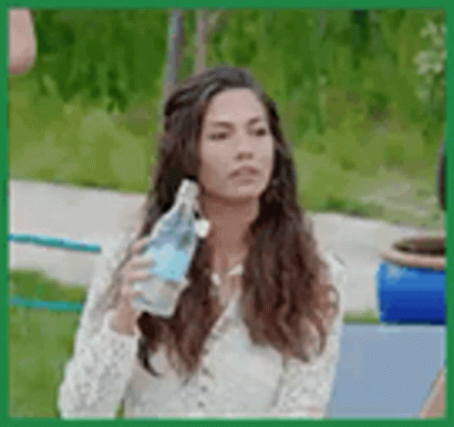 A Woman Is Holding A Bottle Of Water In Her Hand While Sitting On A Bench . GIF