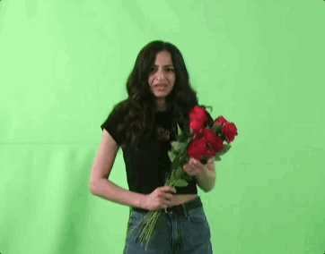 A Woman Is Holding A Bouquet Of Red Roses In Front Of Her Face Against A Green Screen . GIF