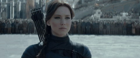 A Woman Is Holding A Bow And Arrow In Front Of A Crowd Of People GIF