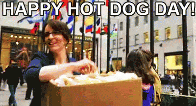 A Woman Is Holding A Box Of Hot Dogs In Front Of A Crowd Of People . GIF