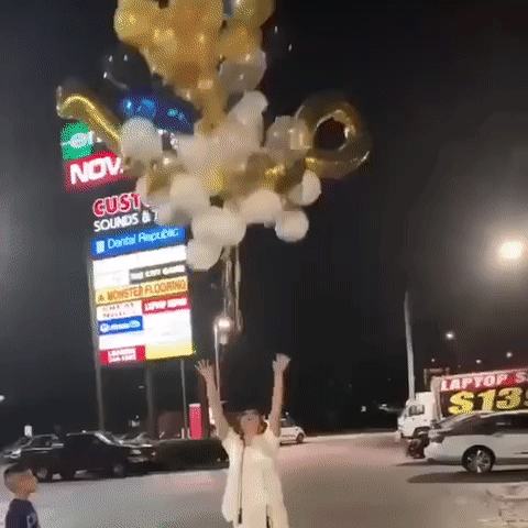 A Woman Is Holding A Bunch Of Balloons In Front Of A Building That Says Gusto Sounds GIF
