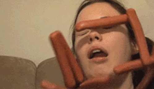 A Woman Is Holding A Bunch Of Hot Dogs To Her Face . GIF