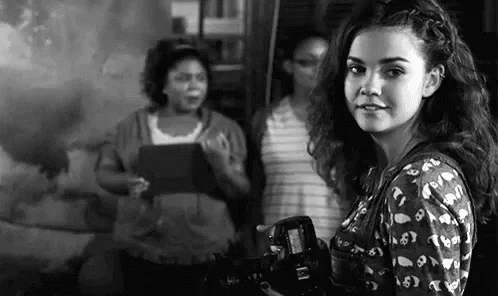 A Woman Is Holding A Camera In Front Of A Group Of Women . GIF