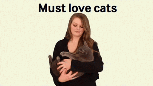 A Woman Is Holding A Cat In Her Arms With The Words Must Love Cats Behind Her GIF