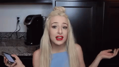 A Woman Is Holding A Cell Phone And Making A Funny Face In A Kitchen . GIF