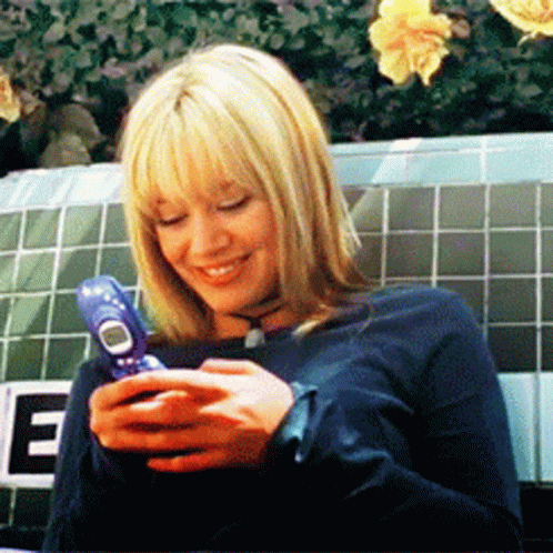 A Woman Is Holding A Cell Phone In Front Of A Sign That Says E GIF