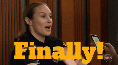 A Woman Is Holding A Cell Phone In Front Of A Sign That Says Finally On It GIF