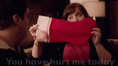 A Woman Is Holding A Christmas Stocking In Front Of Her Face And A Man Is Standing Behind Her . GIF