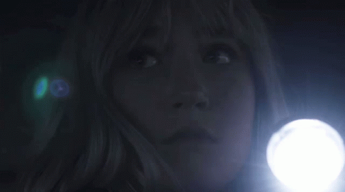 A Woman Is Holding A Flashlight In The Dark And Looking Up . GIF