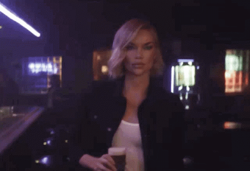 A Woman Is Holding A Glass Of Beer With The Words Hold My Beer Behind Her GIF