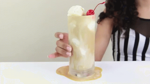 A Woman Is Holding A Glass Of Milkshake With A Cherry On Top GIF