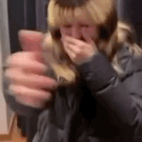 A Woman Is Holding A Glass Of Wine And Covering Her Mouth With Her Hand . GIF