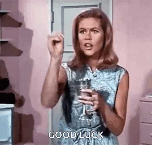 A Woman Is Holding A Glass Of Wine And Giving A Good Luck Sign . GIF