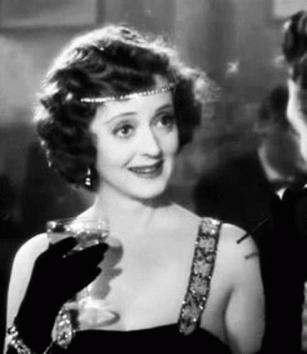 A Woman Is Holding A Glass Of Wine And Smoking A Cigarette . GIF