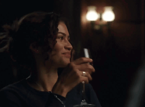 A Woman Is Holding A Glass Of Wine In A Dark Room GIF