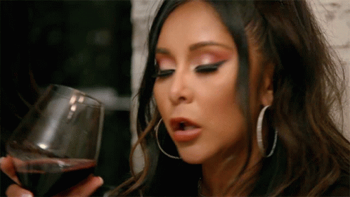 A Woman Is Holding A Glass Of Wine In Her Hand . GIF