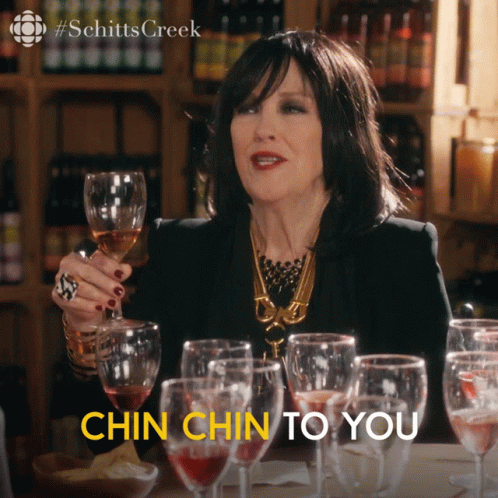 A Woman Is Holding A Glass Of Wine With The Words Chin Chin To You Below Her GIF