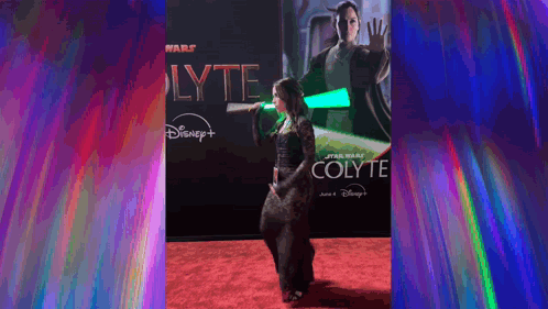A Woman Is Holding A Green Lightsaber On A Red Carpet In Front Of A Poster For Star Wars Colyte . GIF