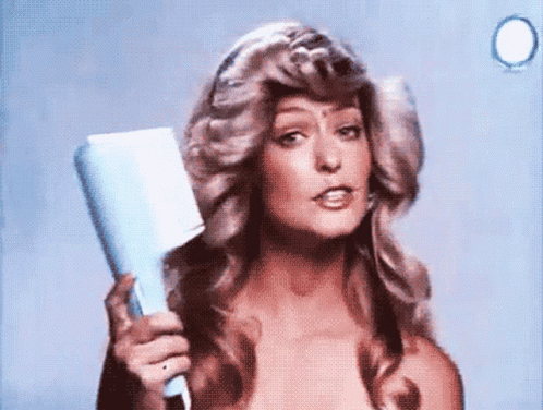 A Woman Is Holding A Hair Dryer In Her Hand And Looking At The Camera GIF