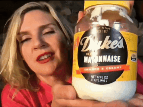 A Woman Is Holding A Jar Of Dukes Mayonnaise GIF