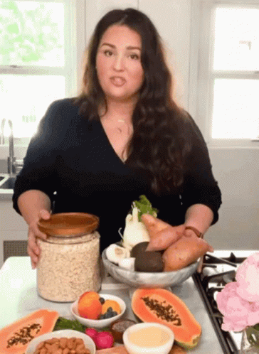 A Woman Is Holding A Jar Of Oatmeal And A Bowl Of Fruit And Vegetables GIF