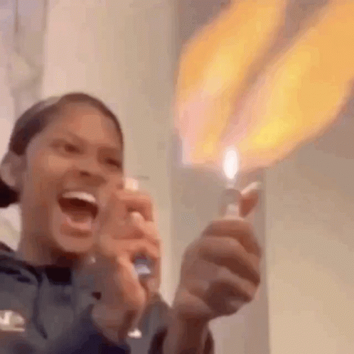 A Woman Is Holding A Lighter With A Flame Coming Out Of It And Laughing . GIF