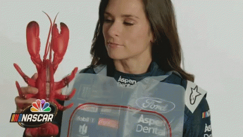 A Woman Is Holding A Lobster In Front Of A Nascar Sign GIF