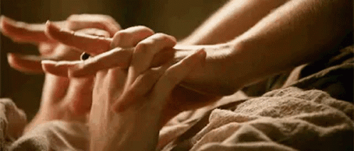 A Woman Is Holding A Man 'S Hand While Laying On A Bed . GIF