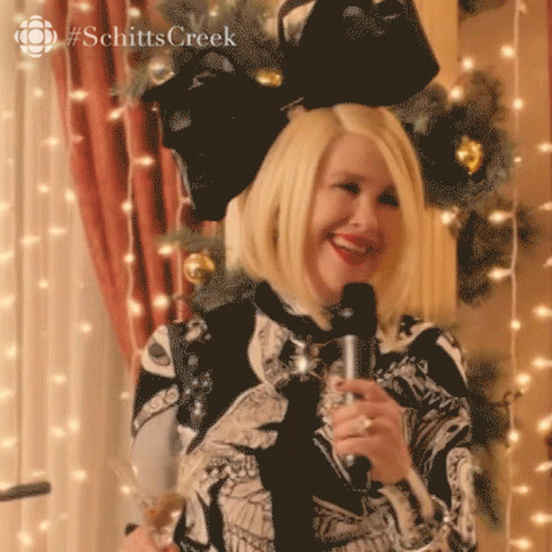 A Woman Is Holding A Microphone And Smiling In Front Of A Christmas Tree .. GIF