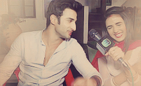 A Woman Is Holding A Microphone And Smiling While A Man Looks On GIF