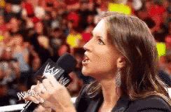 A Woman Is Holding A Microphone In Front Of A Crowd And Talking Into It . GIF