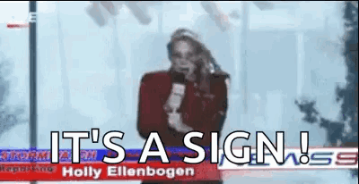 A Woman Is Holding A Microphone In Front Of A Sign That Says `` It 'S A Sign '' . GIF