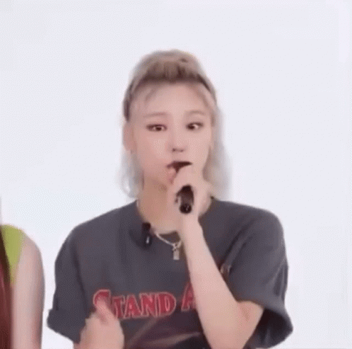 A Woman Is Holding A Microphone In Her Mouth While Wearing A T-Shirt With The Word Stand On It . GIF