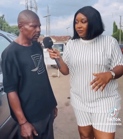 A Woman Is Holding A Microphone While Talking To A Man With A Black Shirt That Says D On It GIF