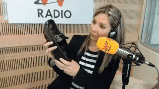 A Woman Is Holding A Pair Of Shoes In Front Of A Microphone In Front Of A Sign That Says Radio GIF