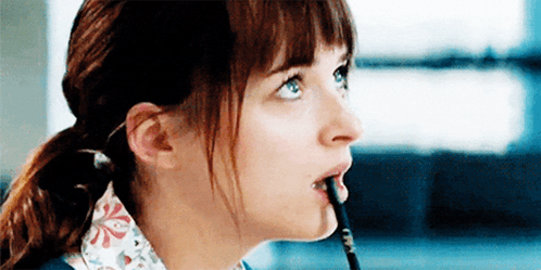 A Woman Is Holding A Pencil In Her Mouth . GIF