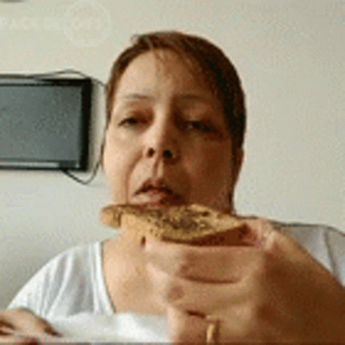 A Woman Is Holding A Piece Of Bread In Front Of Her Face . GIF