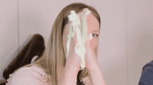 A Woman Is Holding A Piece Of Green Slime In Her Hands In Front Of Her Face . GIF