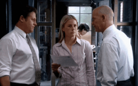 A Woman Is Holding A Piece Of Paper In Her Hand While Talking To Two Men GIF